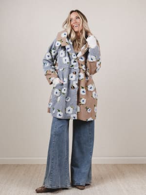 Woman wearing a floral coat and jeans against a plain background