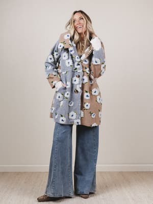 Woman wearing a floral coat and jeans against a plain background