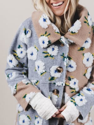 Person wearing a floral patterned coat with white gloves against a neutral background