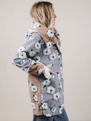 Woman wearing a gray cardigan with floral patterns on a plain background