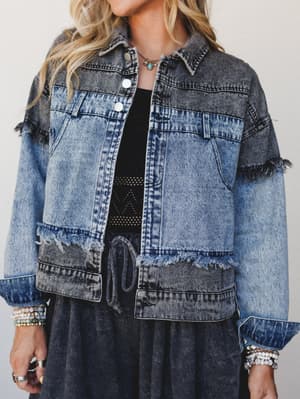 A two-tone acid wash denim jacket with frayed trim detailing, styled open over a black crochet top and charcoal skirt — lived-in and expressive with a boho edge.