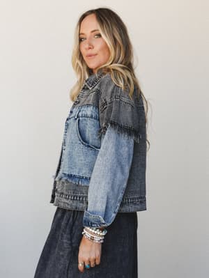 A two-tone denim jacket with raw fringe detailing at the yoke steals the show here — styled over a dark maxi skirt and stacked with beaded bracelets and rings for that effortless, collected boho feel.
