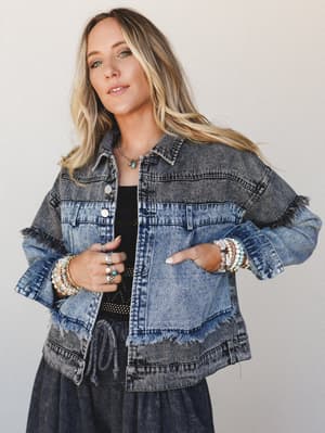 A two-tone acid wash denim jacket with raw fringe trim panels steals the shot — layered over a black tiered skirt and styled with stacked beaded bracelets and a turquoise pendant necklace, it's the kind of piece that makes a casual outfit feel intent