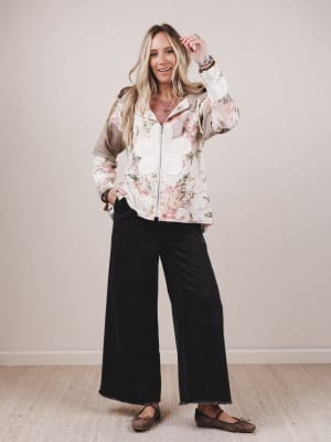 Woman wearing a floral blouse and black pants against a plain background