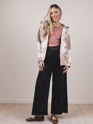 Woman wearing a floral jacket, pink top, and black pants on a plain background