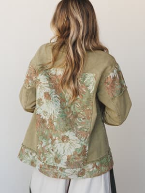 Shot from behind, this olive denim jacket steals the scene with its large-scale floral tapestry panels covering the back, hem, and sleeves — the kind of piece that makes people stop you mid-sentence to ask where you got it.