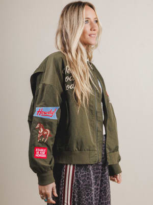 Woman wearing a green bomber jacket with patches on a plain background