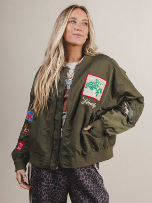 Woman wearing a green bomber jacket with patches on a plain background