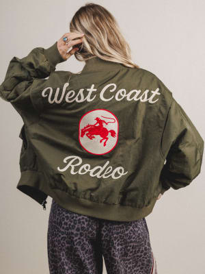 Person wearing a green jacket with 'West Coast Rodeo' text and logo on a plain background