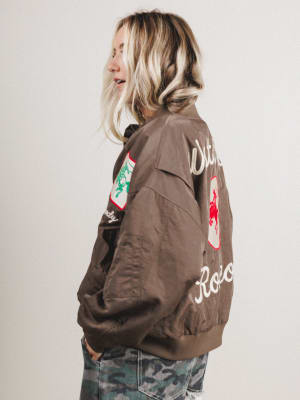 Side view of woman wearing a brown jacket with patches and text, standing against a plain background