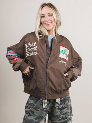 Woman wearing a brown jacket with 'West Coast Rodeo' text and logos on a plain background