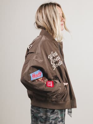 Person wearing a brown jacket with patches and text on a plain background