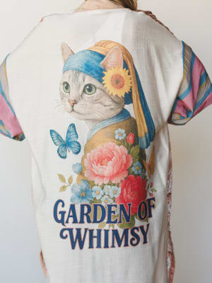 A close back-facing shot of a relaxed kimono-style top in cream, featuring a whimsical illustrated graphic of a cat dressed as Vermeer's 'Girl with a Pearl Earring,' surrounded by peonies, forget-me-nots, a sunflower, and a blue butterfly — with 'Gar