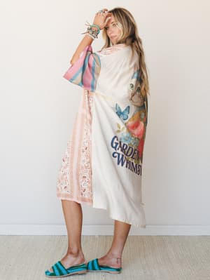 A breezy midi-length kimono with a whimsical cat-and-floral graphic on the back, mixed with eyelet lace and colorblock sleeves — styled with stacked turquoise bracelets and crochet slides for a look that feels like a good mood dressed up.