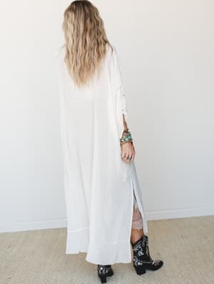 Shot from behind, a model in a floor-length cream kimono with open sides and stud detailing pairs the flowy layer over a blush lace slip and finishes with embroidered black western boots — the whole look has that effortless, slightly undone energy th