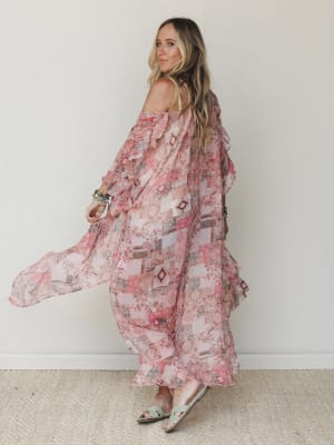 A flowy maxi kimono in a rosy patchwork print catches movement as the model glances back over her shoulder — the kind of piece that looks equally at home over a swimsuit or a slip dress.