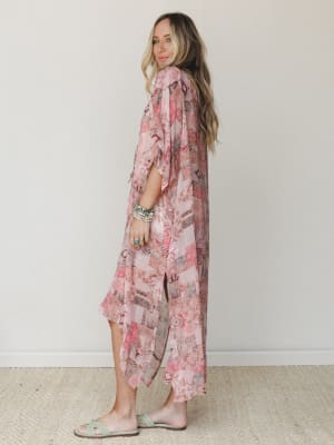 A flowy patchwork-print kimono in blush and rose tones styled over wide-leg pants, shot in profile against a soft neutral wall — effortless and a little dreamy, like something you'd grab on the way out the door and never want to take off.