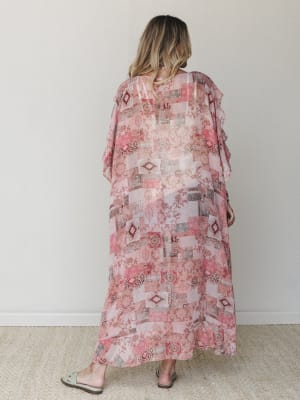 A sheer, floor-length kimono in a rosy patchwork print photographed from the back — the kind of piece that floats when you walk and makes even a Tuesday feel a little more intentional.