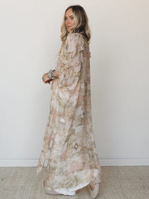 A flowy maxi kimono duster in a soft patchwork-inspired print layers over white underneath — effortlessly romantic, styled with turquoise stacked bracelets and woven wedges for that perfectly collected boho look.