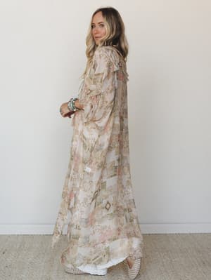 A flowy maxi kimono duster in a soft patchwork-inspired print layers over white underneath — effortlessly romantic, styled with turquoise stacked bracelets and woven wedges for that perfectly collected boho look.