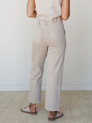 A back-view shot of wide-leg, high-waist pants in a washed ash mocha tone, styled with a cream ribbed top and chain-detail sandals — easy, collected dressing at its most wearable.
