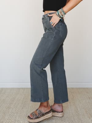 A side-profile shot of wide-leg cropped pants in a washed charcoal denim, styled with a black crop top, leopard print espadrille flatforms, and a stack of boho bracelets — casual and collected with just enough personality.