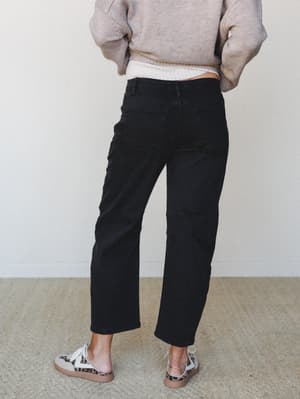 Shot from behind, she's styled in black barrel-leg jeans with visible seam paneling, paired with a cozy oatmeal knit sweater and leopard-print sneakers — the kind of effortless everyday outfit that looks like it came together without trying.