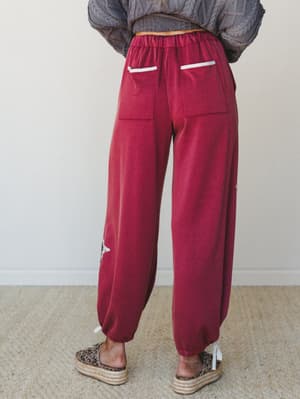 A back-view shot of relaxed jogger-style pants in deep magenta, styled with a chunky cable-knit sweater and leopard print platform espadrilles — the kind of outfit that makes a couch day feel intentional.