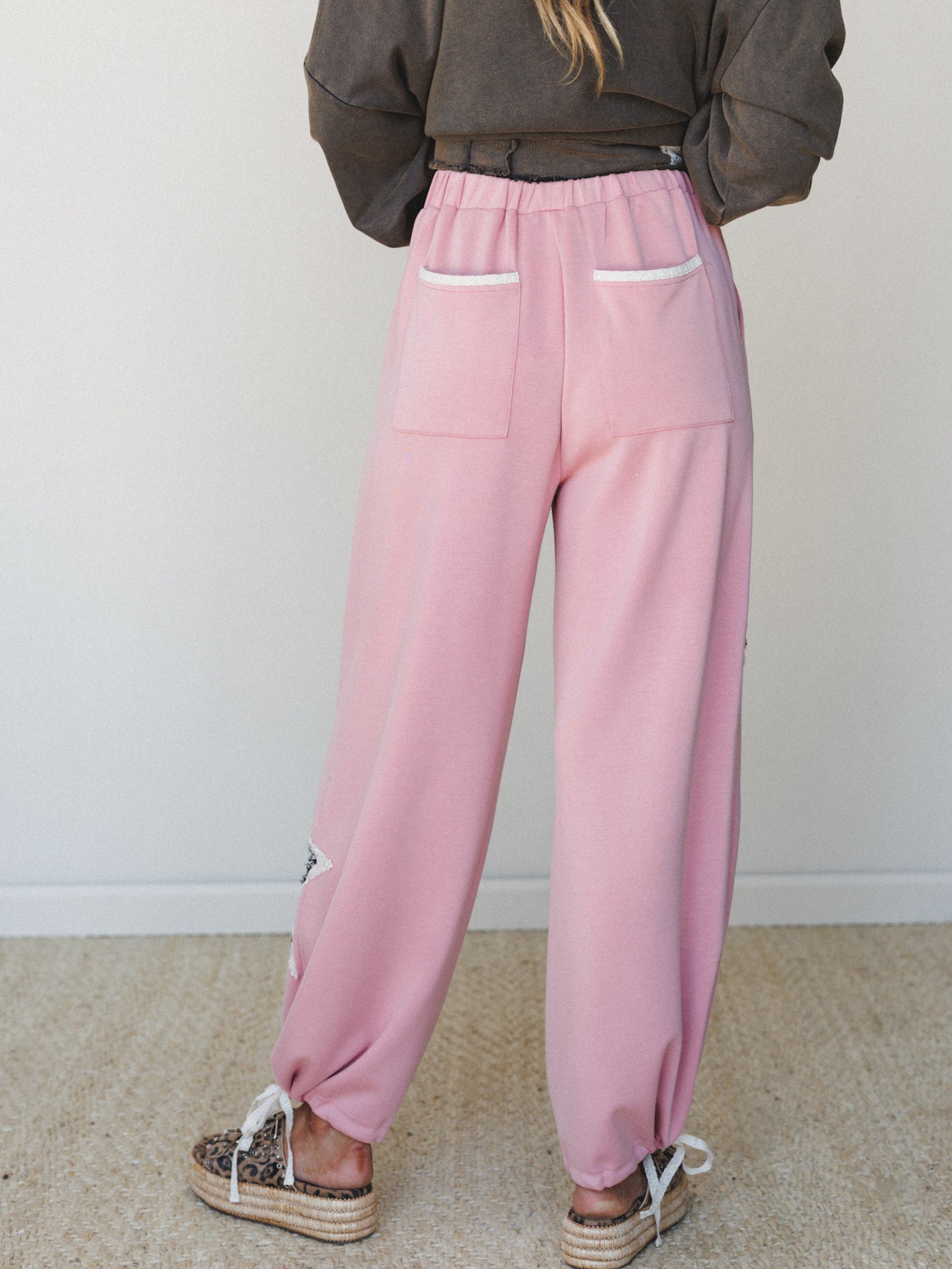 A back-view shot of roomy pink wide-leg sweatpants styled with a washed olive cropped sweatshirt and leopard print platform espadrilles — relaxed and a little unexpected in the best way.