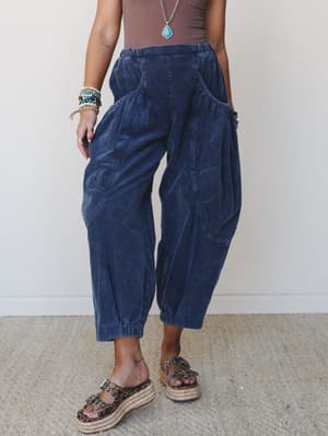 Wide-wale corduroy barrel pants in a deep denim blue, styled with a mauve tank, turquoise pendant necklace, stacked boho bracelets, and espadrille platform sandals — the kind of outfit that looks effortless but clearly wasn't an accident.