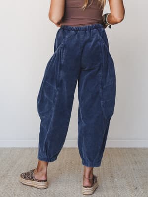 A back-view shot of wide-leg barrel corduroy pants in a deep denim blue, styled with a brown tank and leopard print espadrille platforms — relaxed, expressive, and very much the pants you wear on purpose.