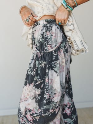 A close-up torso shot of wide-leg floral denim pants with a gathered barrel silhouette, styled with a cropped cream knit top and layered turquoise and silver jewelry — the kind of outfit that looks effortless but absolutely has a whole personality.