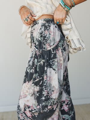 A close-up torso shot of wide-leg floral denim pants with a gathered barrel silhouette, styled with a cropped cream knit top and layered turquoise and silver jewelry — the kind of outfit that looks effortless but absolutely has a whole personality.