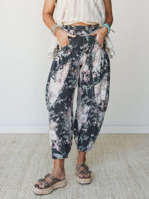 A bold floral barrel-leg pant in washed black denim is styled with a cream textured crop top, platform espadrille sandals, and layered turquoise and beaded bracelets — relaxed, expressive, and completely its own thing.