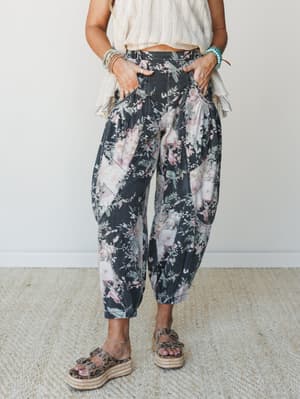 A bold floral barrel-leg pant in washed black denim is styled with a cream textured crop top, platform espadrille sandals, and layered turquoise and beaded bracelets — relaxed, expressive, and completely its own thing.