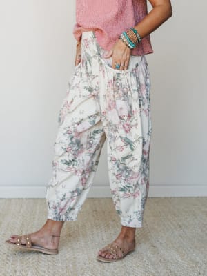 A relaxed floral barrel-leg pant in cream with a botanical bird print styled with a red gingham top, stacked turquoise bracelets, and studded slide sandals — the kind of outfit that feels effortless but clearly thought-through.
