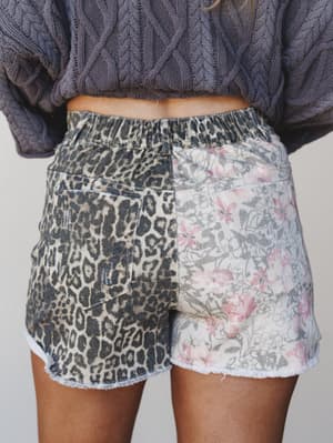 A close-up back view of mixed-print shorts featuring a split design — leopard print on one side, soft floral on the other — paired with a chunky cable-knit sweater for an effortlessly eclectic, cozy-cool look.