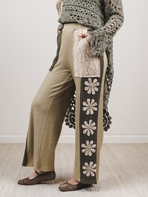 Person wearing a patterned sweater and pants with floral designs on a neutral background