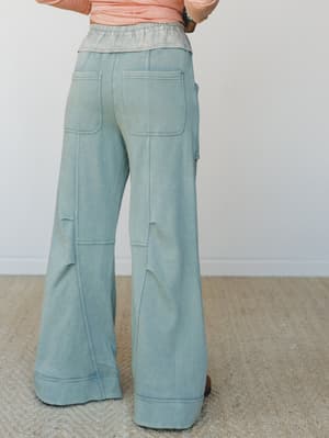 Back view of wide-leg flare sweatpants in a washed sage-teal colorway, styled with a peach long-sleeve top — the kind of pants that feel like sweats but look like a whole outfit.