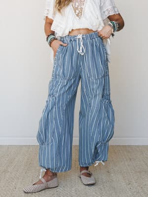 Wide-leg striped pants in a faded indigo and cream print styled with a white lace crop top, layered bead bracelets, and woven flats — effortless and a little free-spirited, like she's already on vacation.