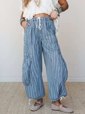 Wide-leg striped cargo pants in a soft blue and cream paired with a white lace crop top and woven flats — effortless and a little unexpected, like someone who packed perfectly for a summer trip.