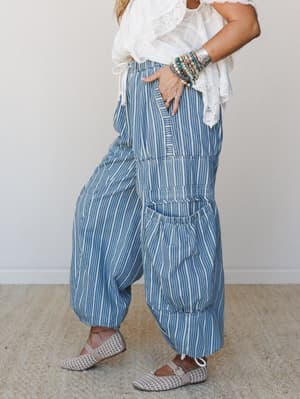 A relaxed side-profile shot of wide-leg striped pants in light denim and cream, styled with a white lace-trim top, stacked beaded bracelets, and woven flats — the kind of outfit that looks effortless but definitely wasn't an accident.
