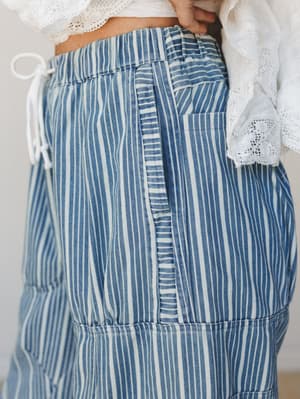 A close-up detail shot of striped wide-leg pants in light denim paired with a white lace crop top, highlighting the drawstring waistband and patch pocket construction.