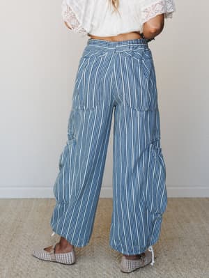 A back-view shot of wide-leg striped pants in soft blue and cream, styled with a white lace crop top and woven flats — relaxed and expressive in the best way.