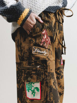 Brown jacket with patches and a hand holding it against a white background