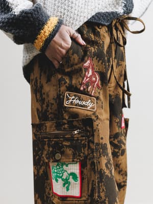 Brown jacket with patches and a hand holding it against a white background