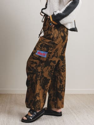 Person wearing camouflage pants with a brand logo on a neutral background