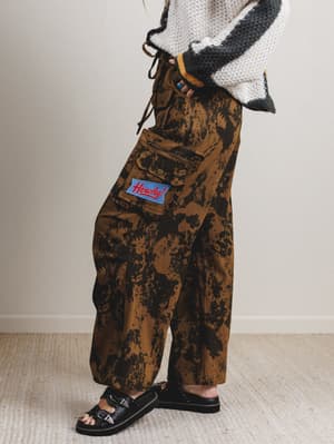 Person wearing camouflage pants with a brand logo on a neutral background