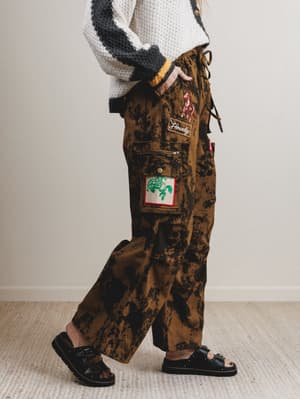 Person wearing camouflage pants with patches on a plain background