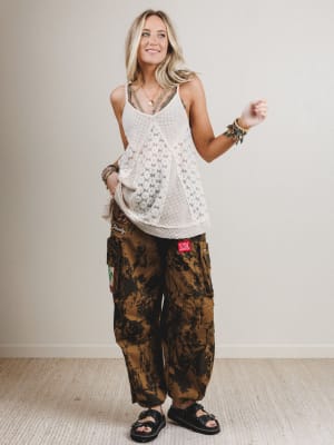 Woman wearing a white sleeveless top and camouflage pants against a plain background